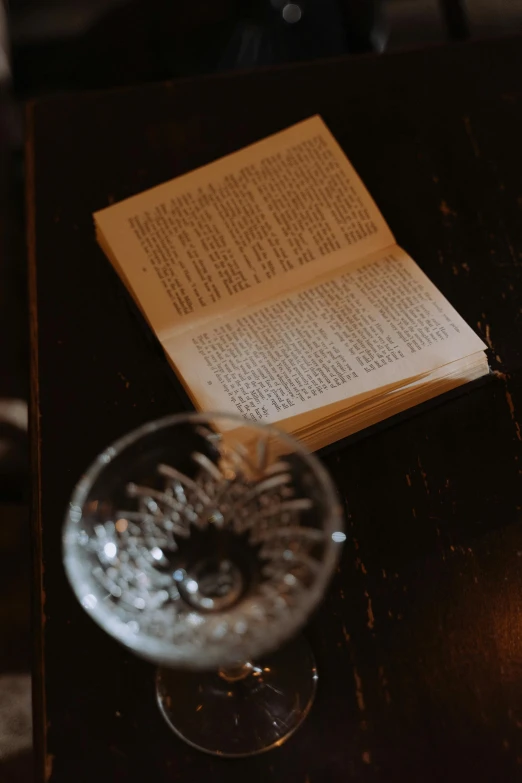 an open book sitting on top of a wooden table, cocktail in an engraved glass, - 6