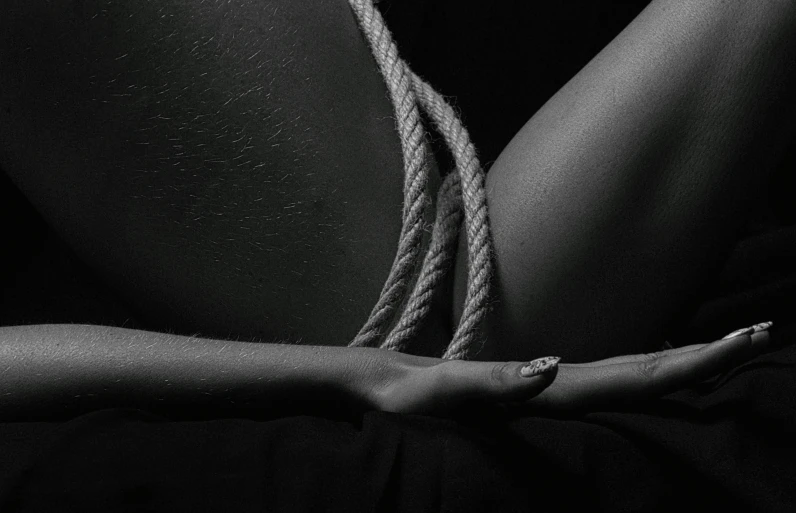 a woman is tied up with a rope, a black and white photo, by Adam Marczyński, unsplash, conceptual art, deep black skin, thighs close up, done in the style of caravaggio, teaser