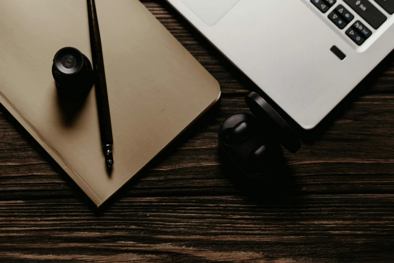 an open laptop computer sitting on top of a wooden desk, by Sebastian Vrancx, trending on pexels, black and brown, table with microphones, sleek round shapes, pen and paper