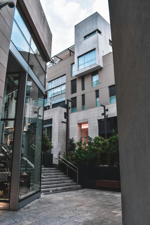 a man riding a skateboard down a sidewalk next to a tall building, stairs to an upper floor, courtyard, restaurant exterior photography, square