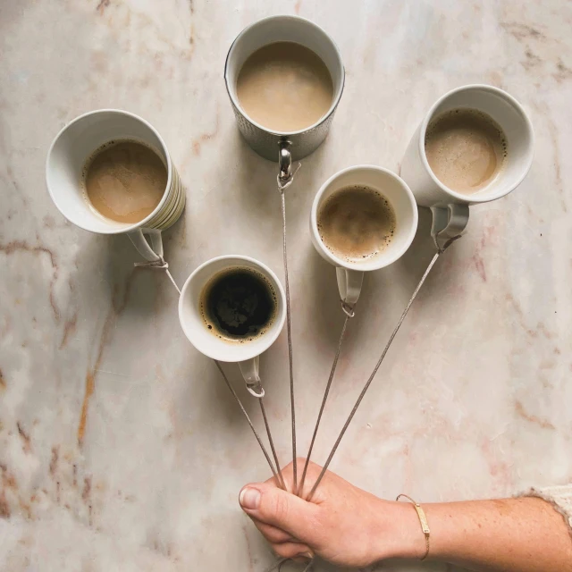 a person holding a bunch of cups of coffee, inspired by Suzanne Duchamp-Crotti, unsplash, silver，ivory, wands, 5, made of glazed