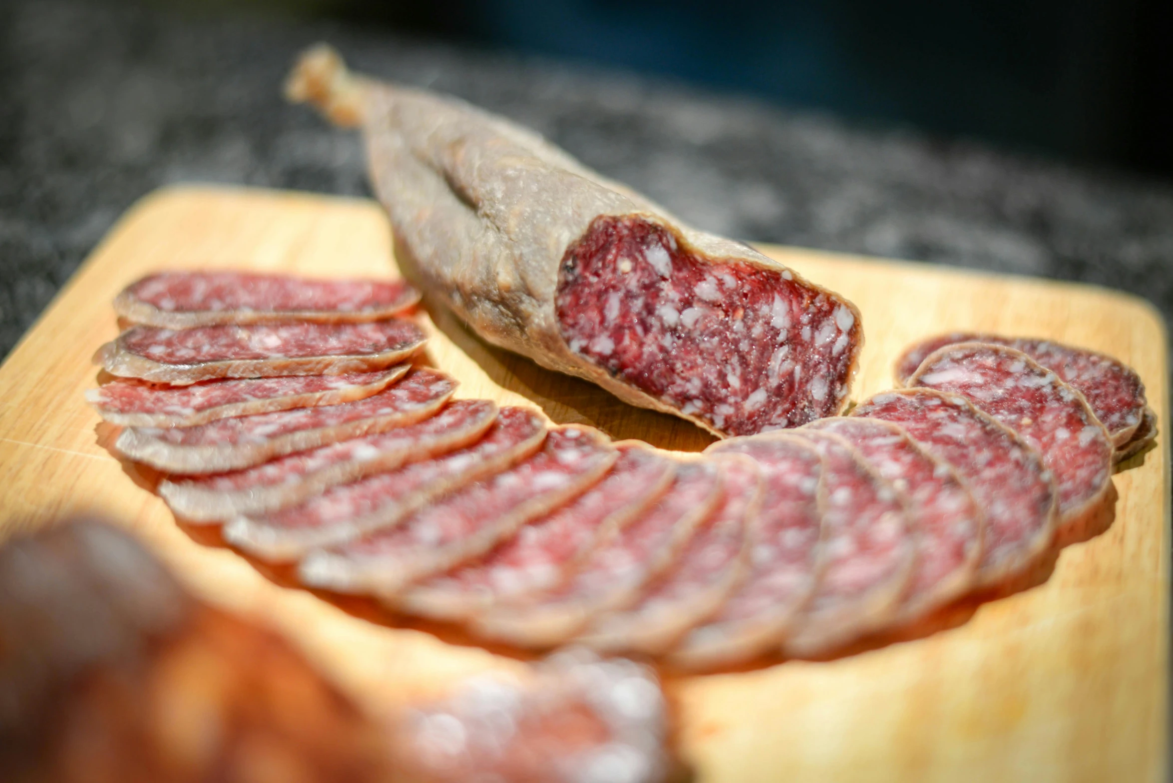 sliced sausage sitting on top of a wooden cutting board, a portrait, by Jessie Algie, pexels, art nouveau, traditional corsican, made of glazed, nice weather, grey