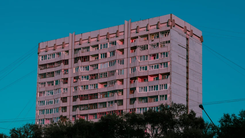 a tall pink building sitting on top of a lush green field, a colorized photo, inspired by Elsa Bleda, pexels contest winner, brutalism, soviet apartment building, low saturated red and blue light, 000 — википедия, glowing windows