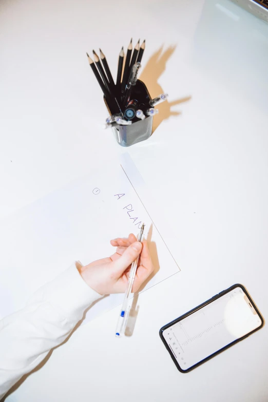 a person writing on a piece of paper on a table, in a white room, flatlay, high-quality photo, fzd school of design