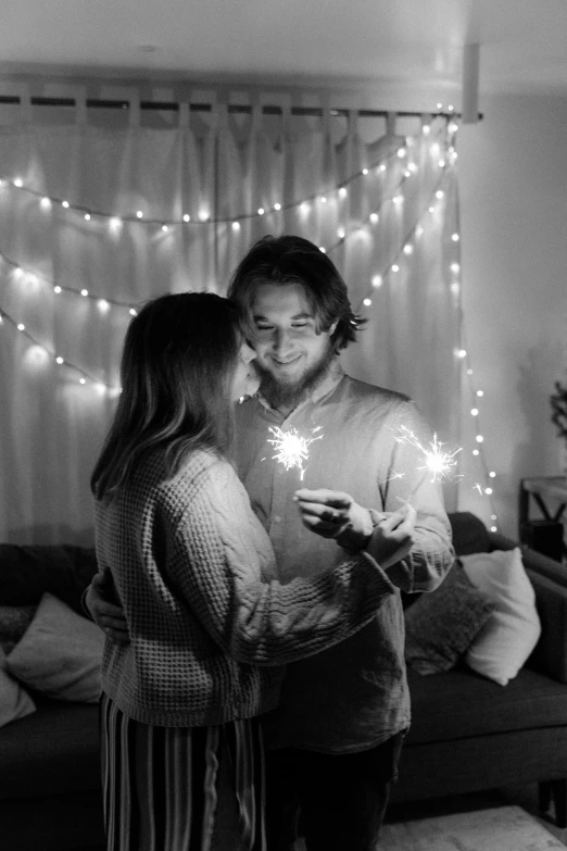 a man and woman standing next to each other in a living room, a black and white photo, pexels contest winner, romanticism, fairy lights, sparklers, fanart, man proposing his girlfriend