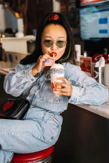 a woman sitting on a stool with a drink in her hand, trending on pexels, wearing double denim, covered in sprinkles, vanessa morgan, red stripe