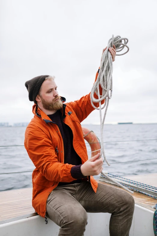 a man sitting on a boat holding a rope, a portrait, inspired by Jóhannes Sveinsson Kjarval, unsplash, orange jacket, seattle, wearing adventuring gear, subreddit / r / whale