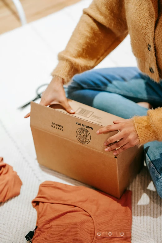 a woman sitting on the floor holding a box, touching her clothes, inside its box, ebay listing thumbnail, opening shot