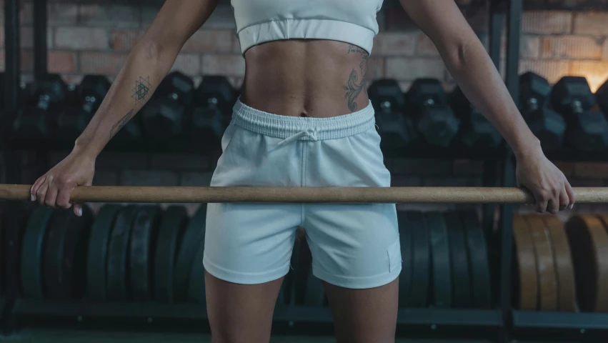 a woman standing next to a bar in a gym, trending on pexels, white fluffy cotton shorts, background image, muscular! crossfit, white and teal garment