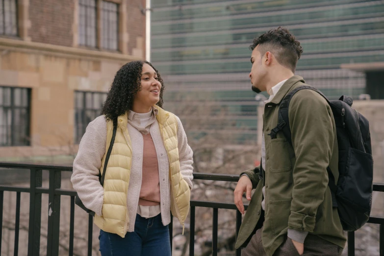 a man and a woman standing next to each other, trending on pexels, happening, college students, talking, wearing jacket, an olive skinned