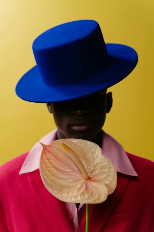a man in a blue hat holding a flower, an album cover, by Nathalie Rattner, pexels contest winner, afrofuturism, adut akech, issey miyake, pink and yellow, juicy color