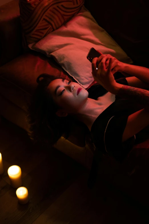 a woman laying on top of a bed next to candles, a portrait, inspired by Nan Goldin, trending on pexels, checking her phone, androgynous vampire, gemma chan, still from a movie
