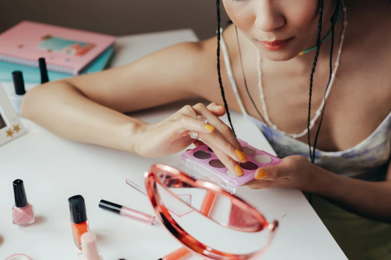 a woman sitting at a table in front of a mirror, an airbrush painting, trending on pexels, with square glasses, pink and orange, flatlay, wolfy nail