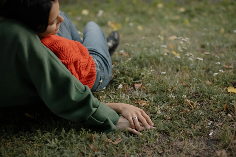 a woman sitting on top of a grass covered field, wearing a green sweater, laying down with wrists together, tiny person watching, ignant