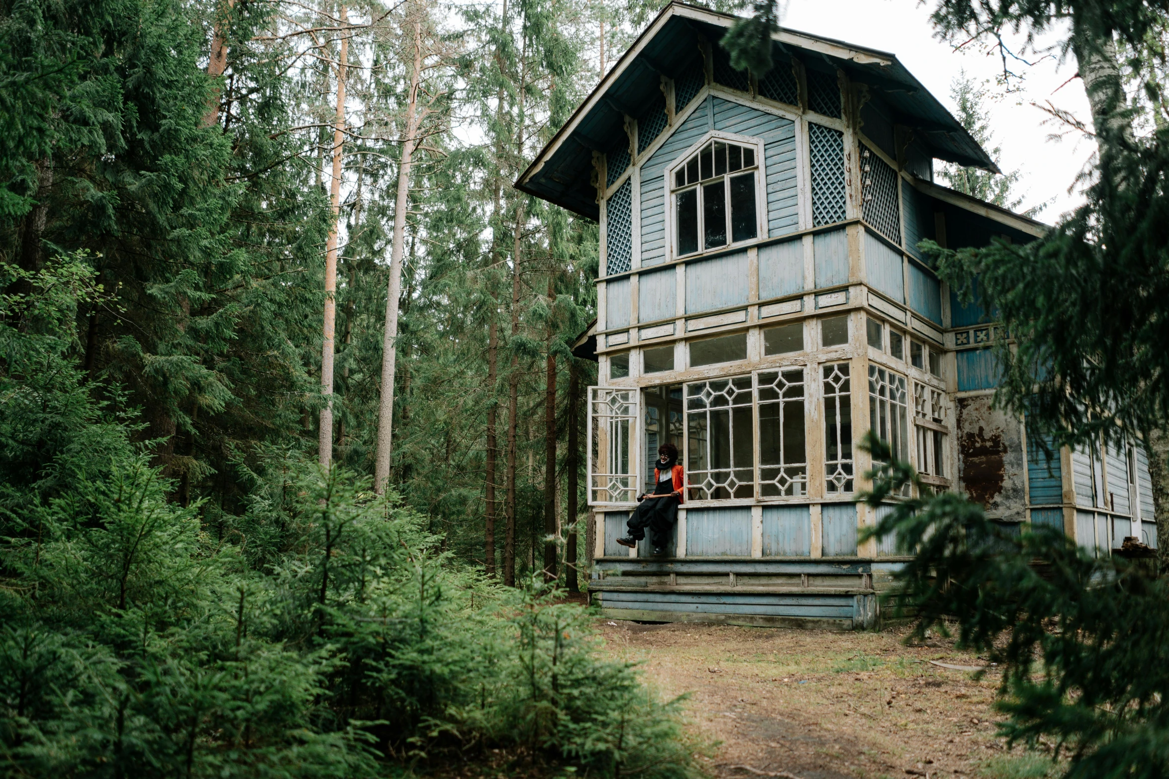 a person standing in front of a house in the woods, by Emma Andijewska, unsplash, art nouveau, russian architecture, sitting in the forrest, tall thin build, summer siberian forest taiga