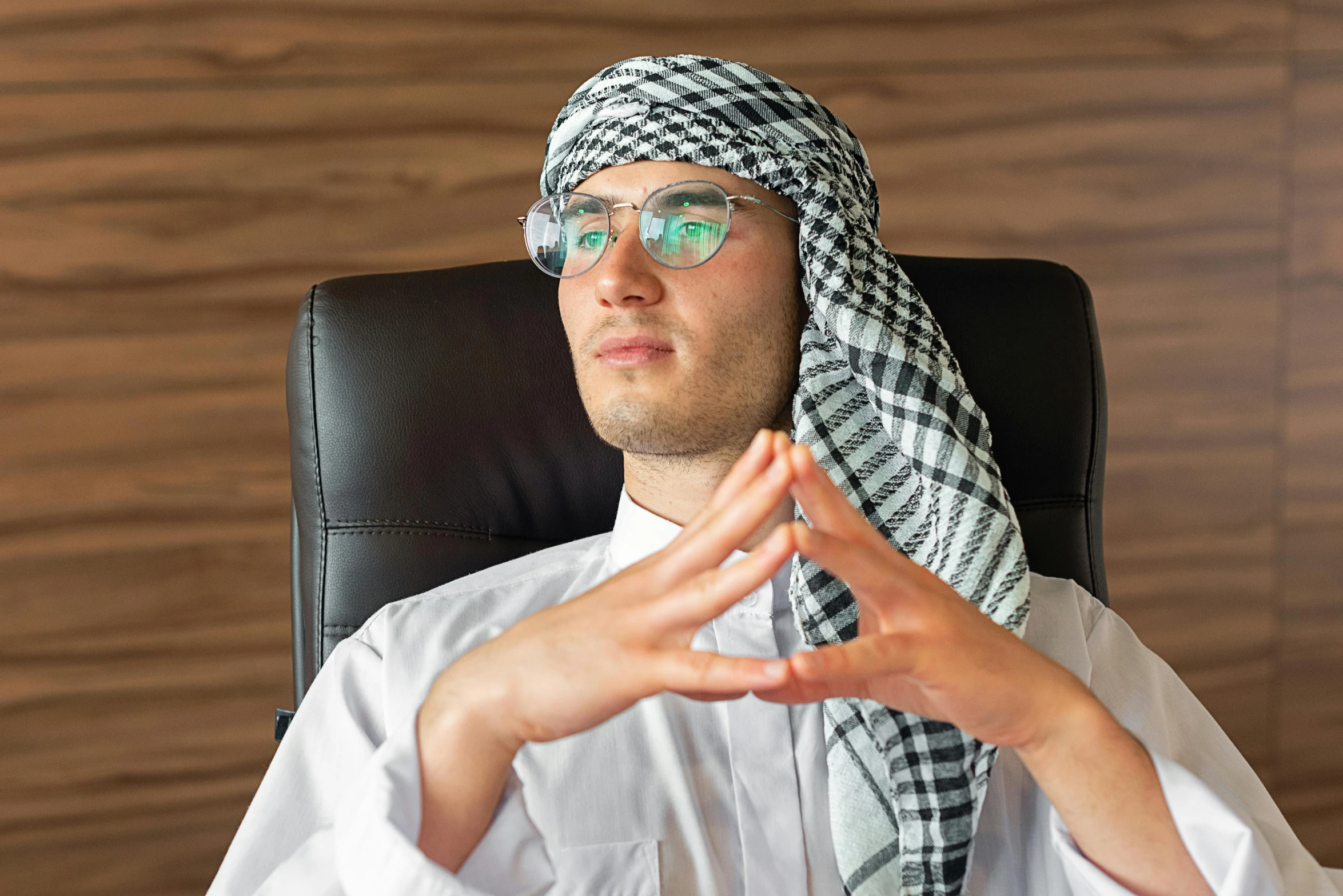 a man sitting in a chair wearing a headscarf, inspired by Sheikh Hamdullah, pexels, hurufiyya, shrugging arms, typical cryptocurrency nerd, corporate boss, traditional clothes