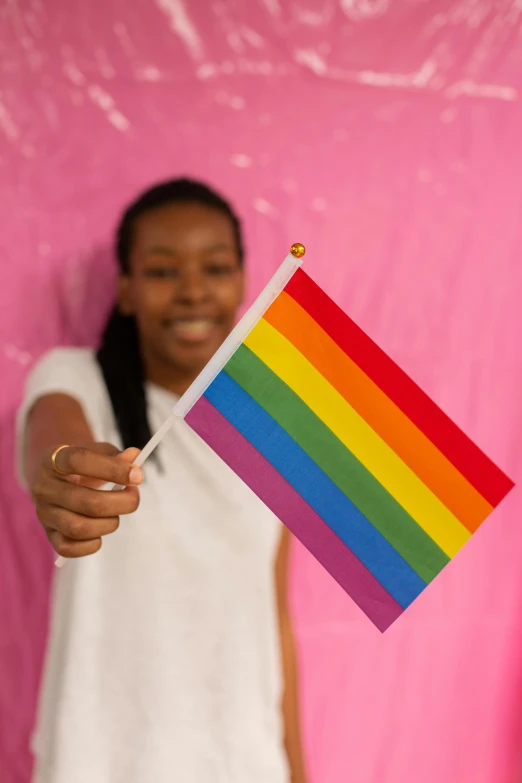 a woman holding a rainbow flag in front of a pink wall, ( ( dark skin ) ), promo image, 19-year-old girl, holding trident