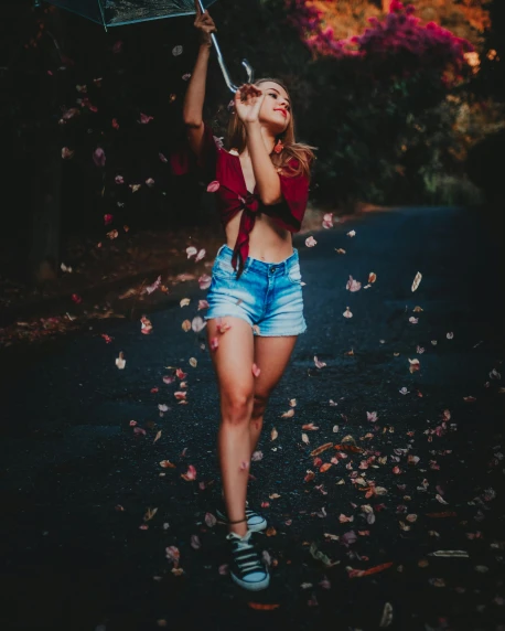 a woman standing in the middle of a road holding an umbrella, a colorized photo, by Robbie Trevino, pexels contest winner, falling red petals, wearing a camisole and shorts, leafs, satisfied pose