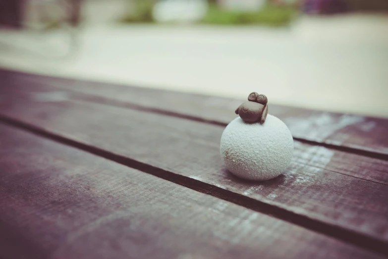 a small figurine sitting on top of a wooden table, by Simon Gaon, unsplash, concrete art, puffballs, snail, sitting on bench, white