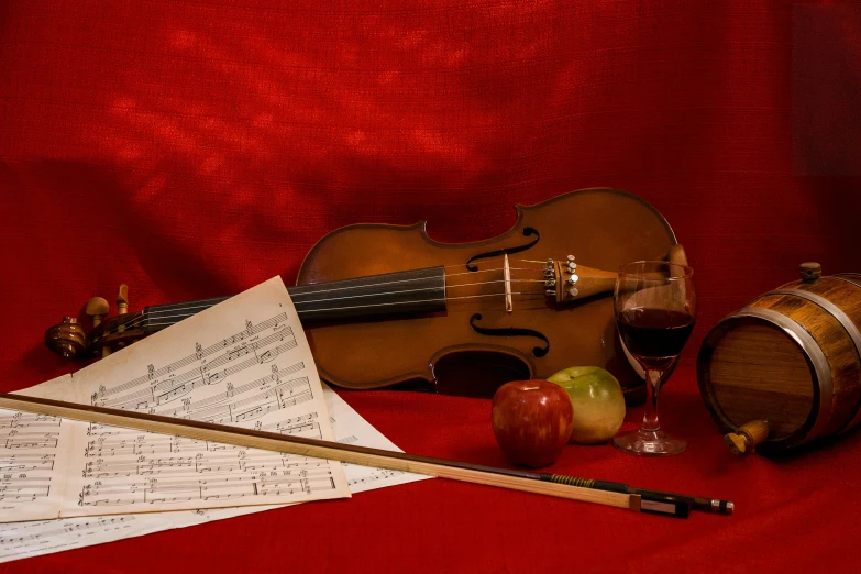 a violin sitting on top of a table next to a glass of wine, a still life, inspired by George Lambourn, pexels, against a red curtain, sheet music, still life of an apple, thumbnail