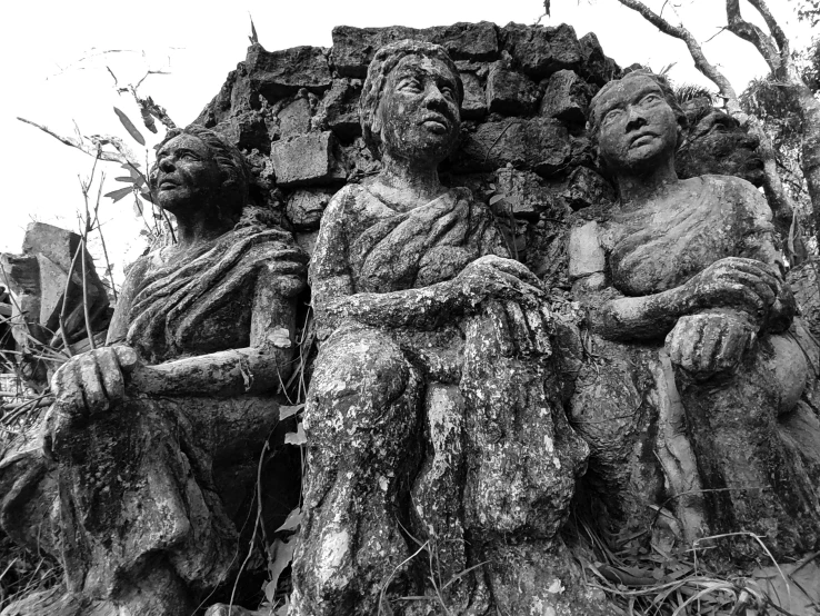 a group of statues sitting on top of a tree, by Sunil Das, humanity's last sacrifice, creepy carved expression, three women, black & white