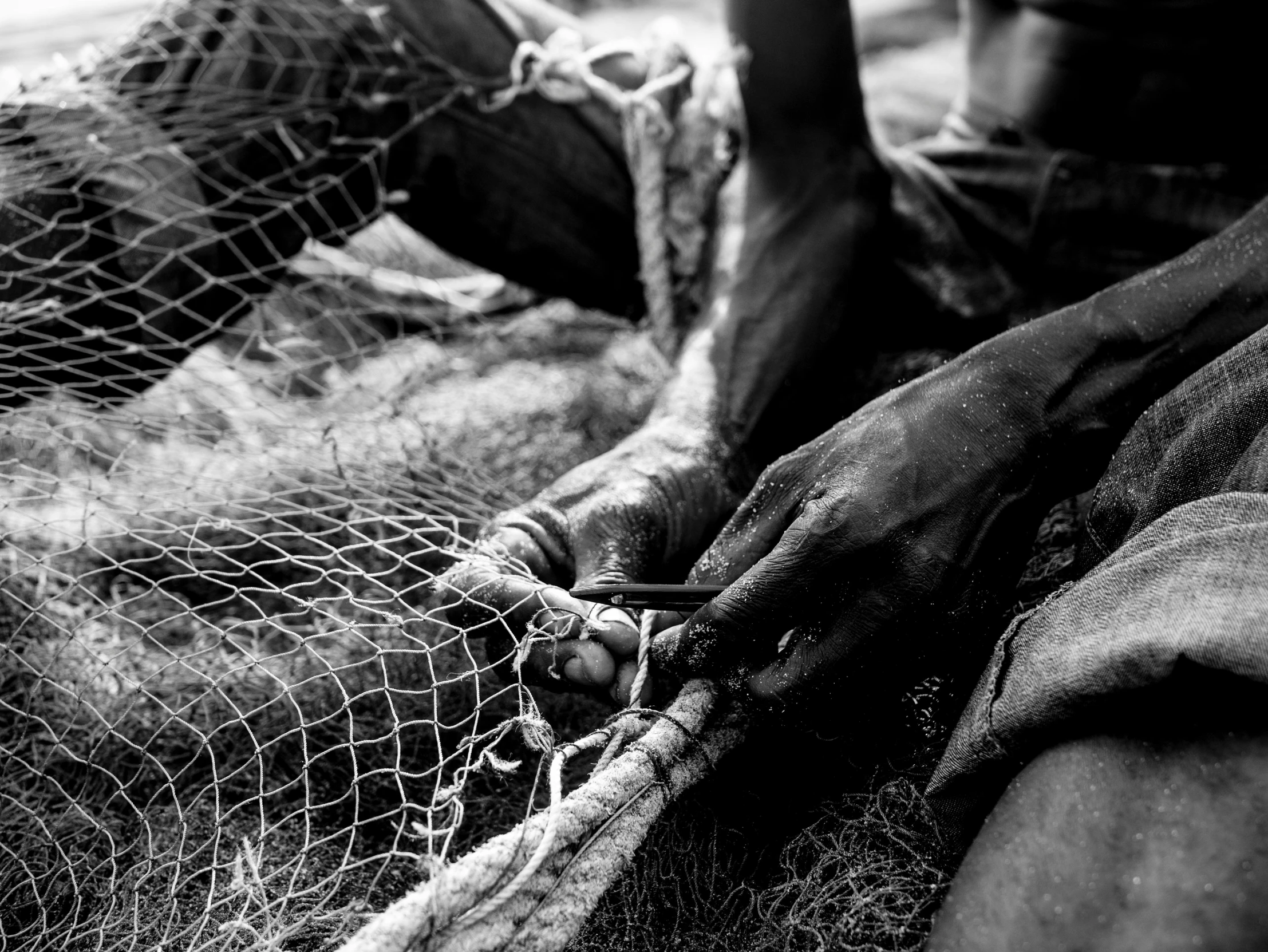 a man laying on the ground next to a net, a black and white photo, by John Hutton, pexels, two hands reaching for a fish, masai, closeup photo, stitching