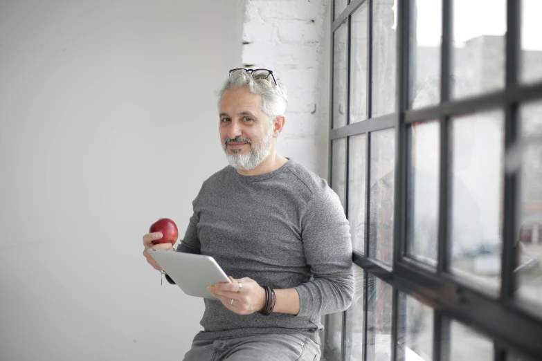 a man sitting on a window sill holding an apple, pexels contest winner, silver hair and beard, 15081959 21121991 01012000 4k, took on ipad, on a white table