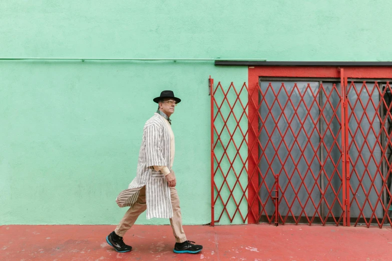 a man walking in front of a green building, an album cover, inspired by Joseph Beuys, pexels contest winner, maximalism, stripes, dressed thobe, los angeles 2 0 1 5, color block