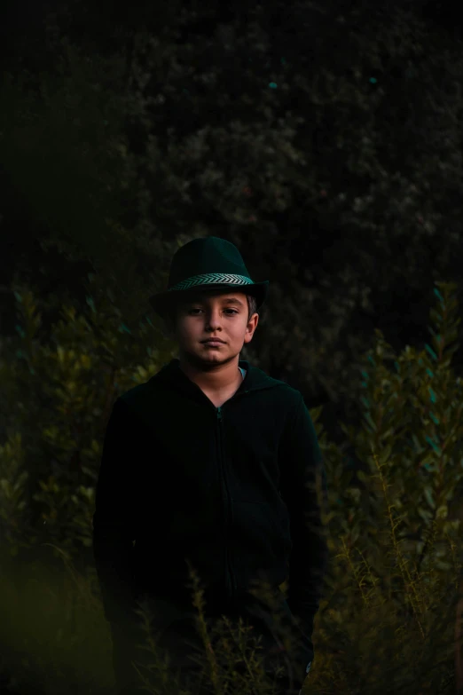 a young man standing in the middle of a forest, an album cover, pexels contest winner, green hat, little kid, with a black background, sayem reza