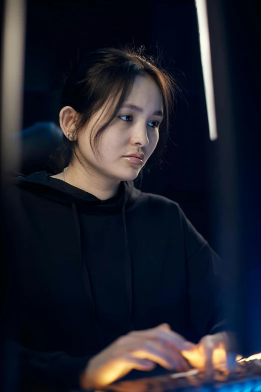 a woman sitting in front of a computer keyboard, inspired by Ayami Kojima, black hoodie techie, looking serious, worksafe. cinematic, female actress from korea