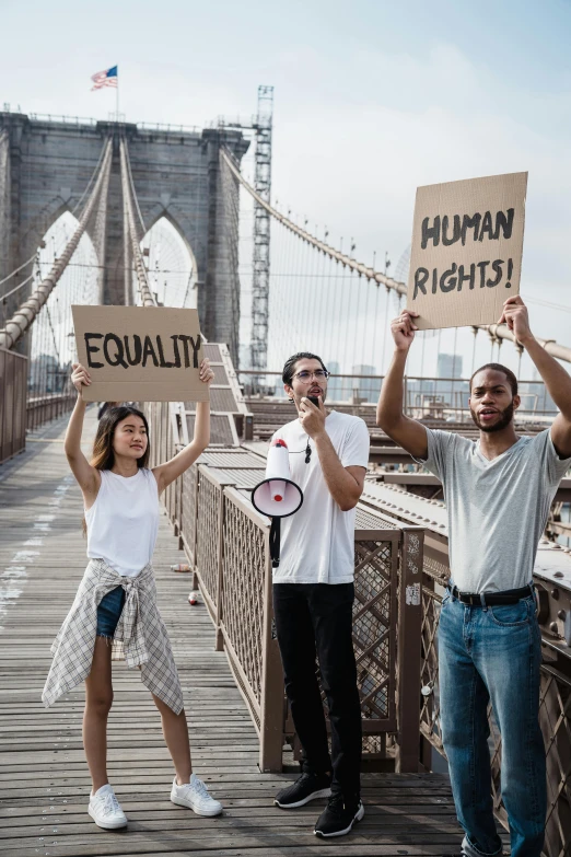 a group of people holding up signs on a bridge, a colorized photo, trending on unsplash, excessivism, harlem, gay rights, three, a person standing in front of a