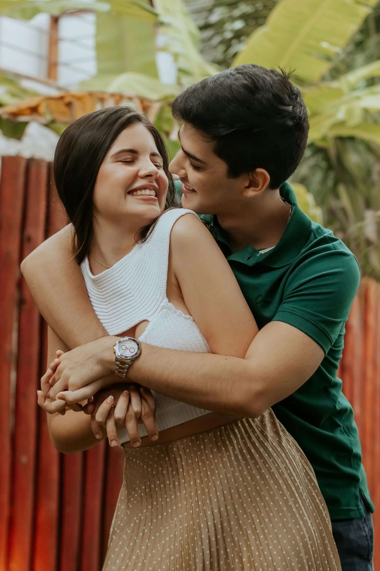 a man and woman hugging each other in front of a fence, a picture, pexels contest winner, latina, smiling playfully, manila, lush foliage