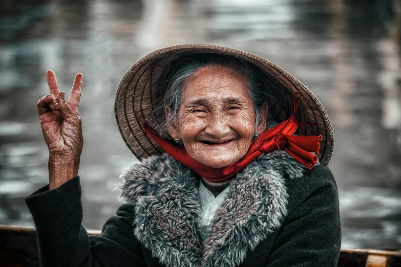 a woman sitting on top of a boat holding up a peace sign, by Joze Ciuha, pexels contest winner, lots of wrinkles, small hat, traditional chinese, warm and happy