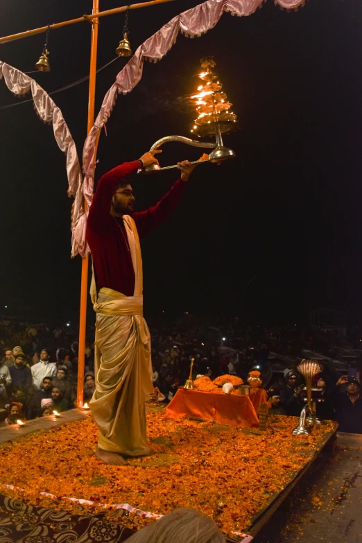 a man standing on top of a bed of flowers, a statue, samikshavad, blessing the soil at night, performing on stage, torches in ground, long orange hair floating on air