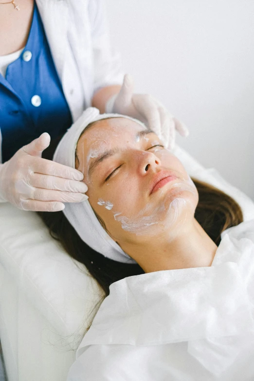 a woman getting a facial mask at a beauty salon, by Nicolette Macnamara, scars on face, grey, synthetic bio skin, clinical