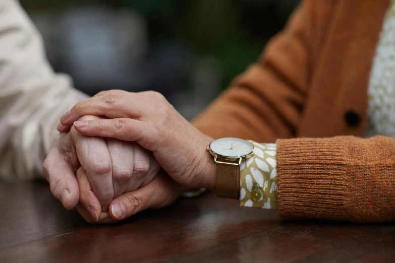 a close up of two people holding hands, by Sylvia Wishart, unsplash, photorealism, sitting on a table, autumnal, folded arms, older woman