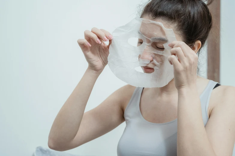 a woman shaving her face in front of a mirror, trending on pexels, plasticien, wearing giant paper masks, with a white background, wearing translucent sheet, facial scar