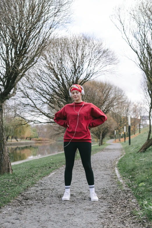 a woman standing on a path with her hands on her hips, inspired by Louisa Matthíasdóttir, pexels contest winner, happening, red hoodie, non-binary, dynamic active running pose, low quality photo