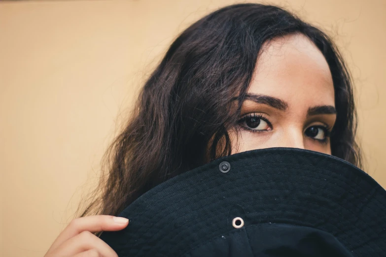 a close up of a person holding a hat, trending on pexels, black sclera, young middle eastern woman, face covers half of the frame, spying discretly