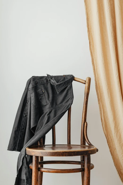 a black jacket sitting on top of a wooden chair, curtains