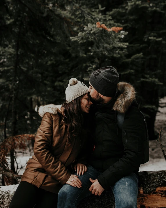 a man and woman sitting on a log in the woods, pexels contest winner, romanticism, wearing a beanie, profile image, kissing smile, cold temperature