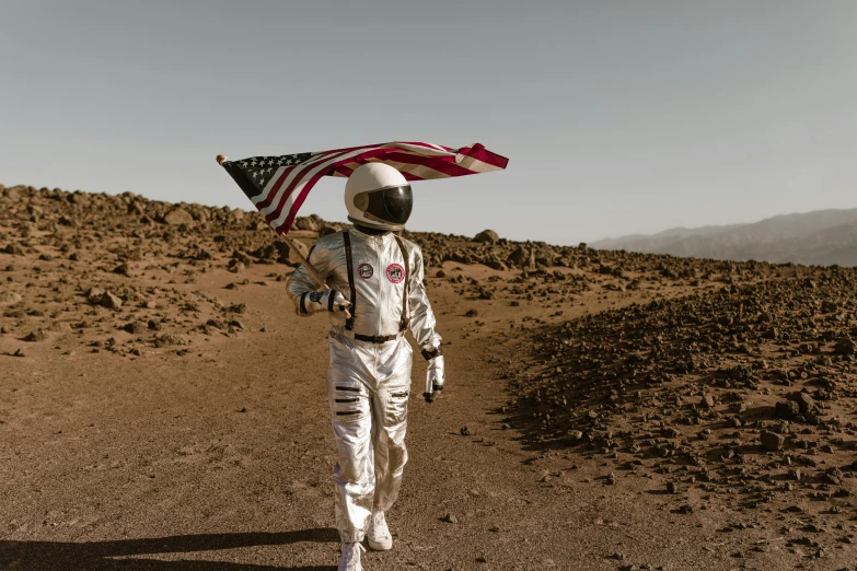 a man in a spacesuit holding an american flag, pexels contest winner, afrofuturism, red desert mars, silver space suit, brown, instagram post