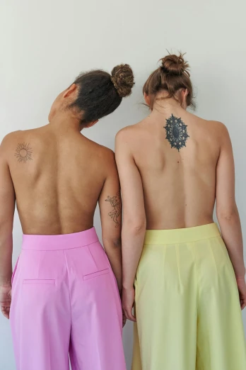 a couple of women standing next to each other, a tattoo, by Jessie Alexandra Dick, antipodeans, nonbinary model, lower back, various colors, meredith schomburg