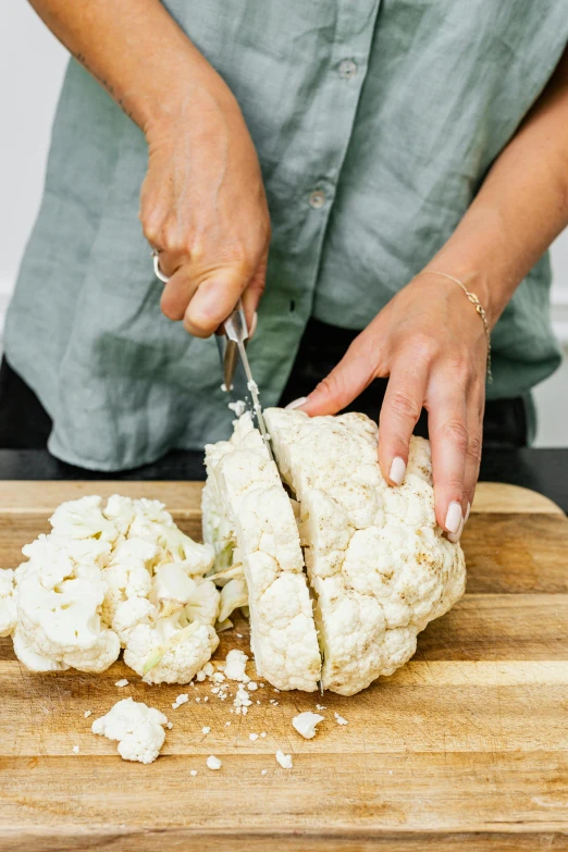 a woman cutting up a piece of cauliflower on a cutting board, by Carey Morris, split in half, fan favorite, cast, big hands