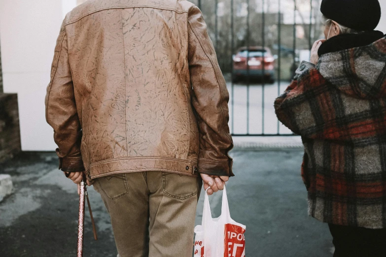 a man and a woman walking down a street, pexels contest winner, brown leather jacket, getting groceries, old man, close-up shot from behind
