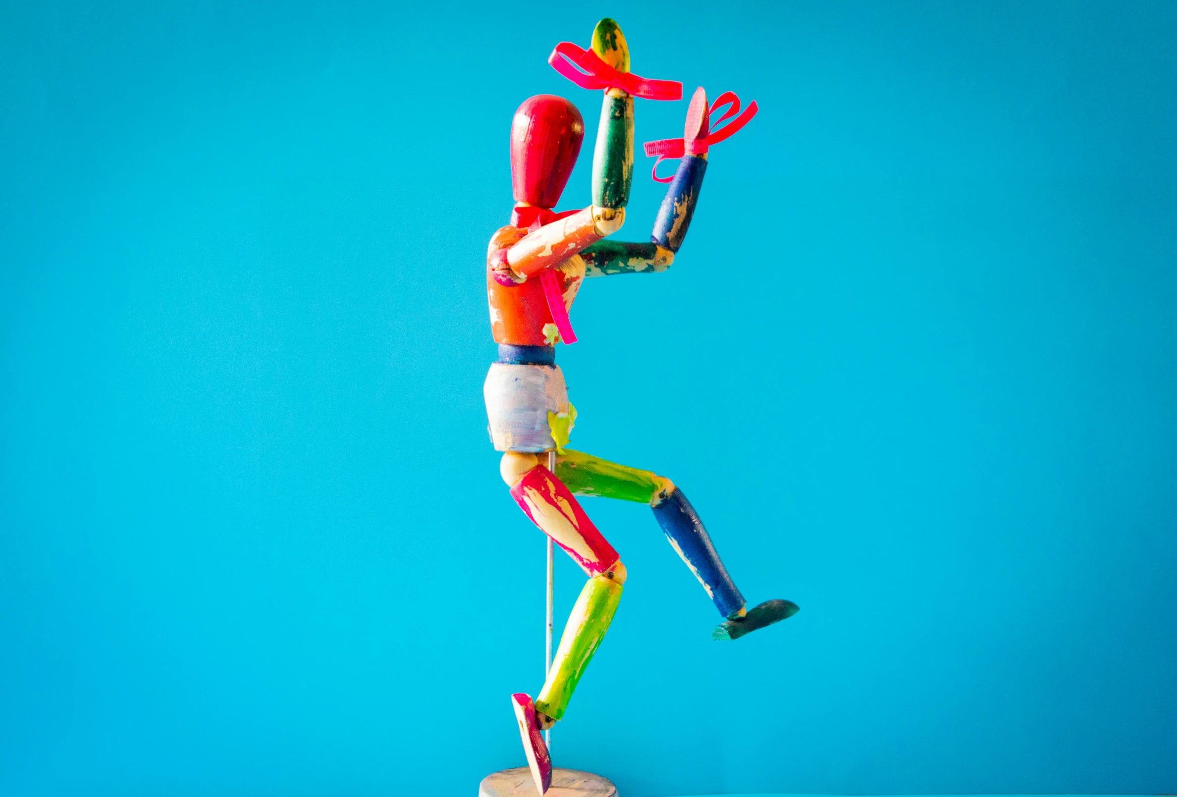 a close up of a figurine on a blue surface, inspired by Sarah Lucas, pexels contest winner, kinetic art, multicoloured, leaping with arms up, giant wooden club, vibrant colour