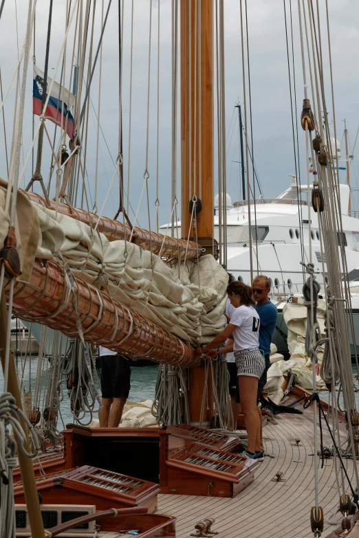 a group of people standing on the deck of a boat, sails and masts and rigging, slide show, sports photo