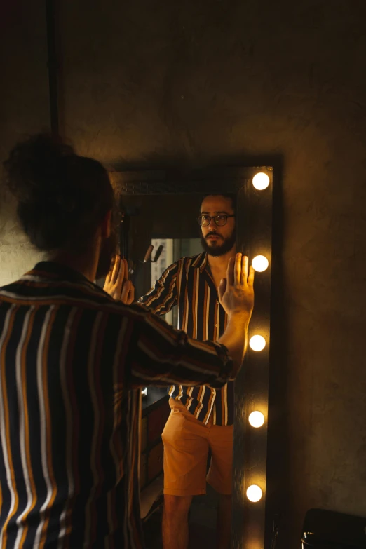 a man that is standing in front of a mirror, inspired by Elsa Bleda, pexels contest winner, wearing stripe shirt, dim lighting, ( ( theatrical ) ), bearded man