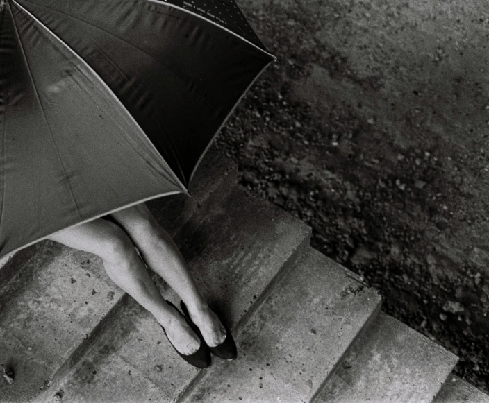 a black and white photo of a woman holding an umbrella, inspired by Sergio Larraín, conceptual art, feet on the ground, stairs, rinko kawauchi, detailed shot legs-up