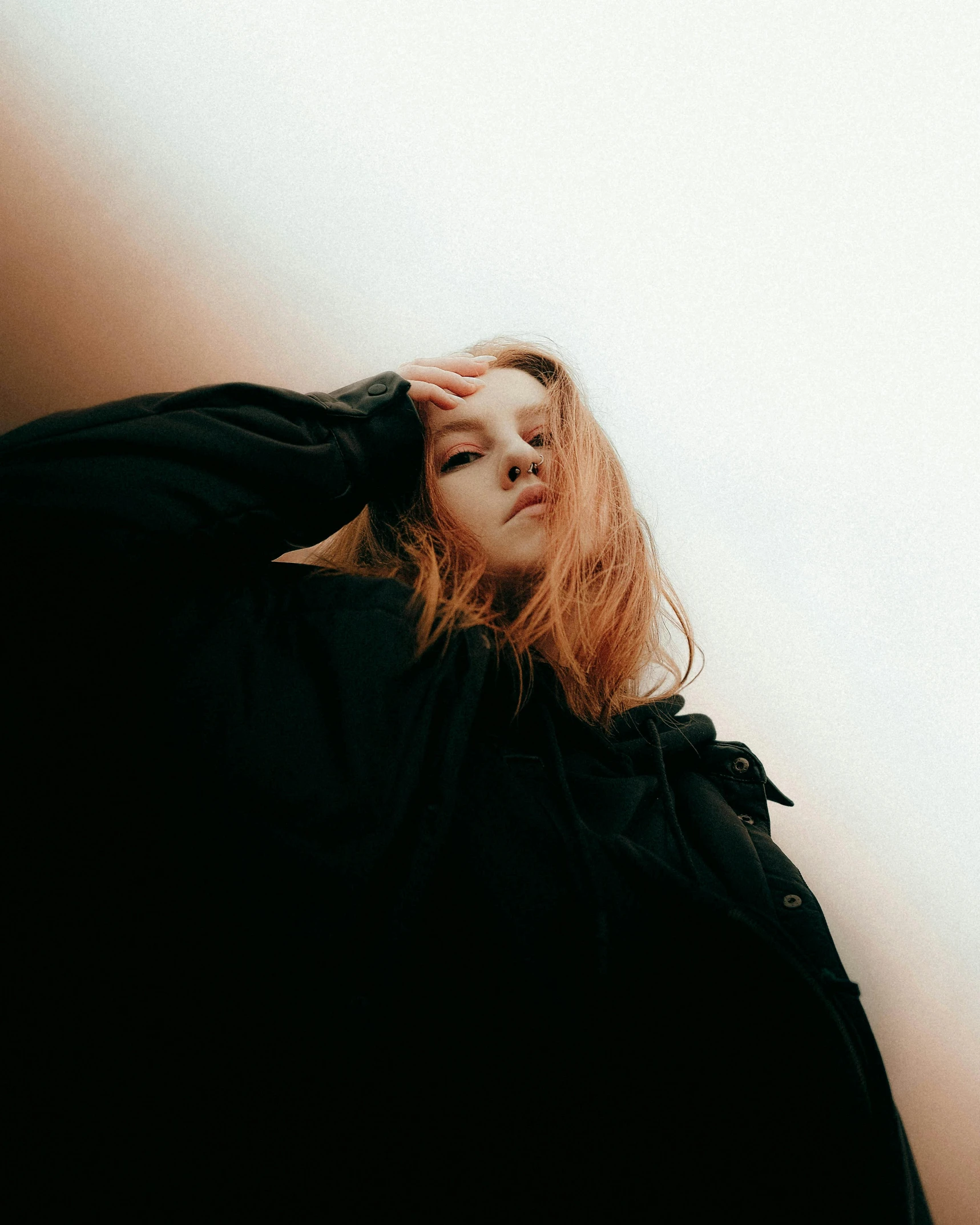 a woman with red hair leaning against a wall, inspired by Elsa Bleda, trending on pexels, realism, wearing a black hoodie, looking up to the sky, she is distressed, sydney sweeney